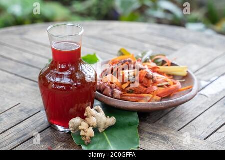 wedang uwuh drinks in glass bottles and red ginger, secang shaved wood, lemongrass in pottery plates,a traditional heritage Javanese of Indonesia Stock Photo