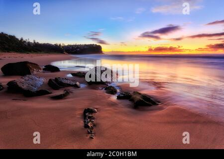 Dark sunrise at sandy NOrthern Beach in Sydney with washed clean sand around rocks between headlands. Stock Photo