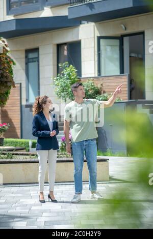 Tall man in jeans pointing to the house and talking to the well-dressed woman Stock Photo