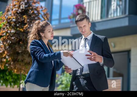 Client in a black suit scrutinizing the contract, broker assisting him Stock Photo