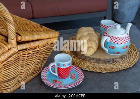 High tea picnic concept with decorated tea pot, teacups and picnic basket on a table Stock Photo