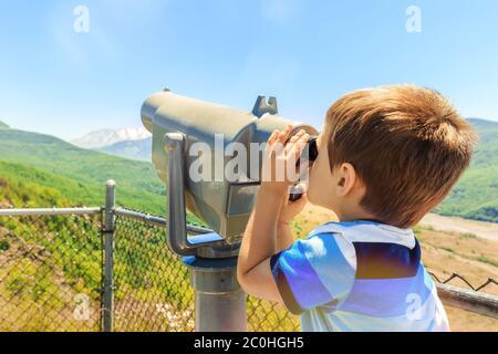 Little boy using telescope to see Mount St. Helens peak from observation point, Washington state, USA Stock Photo