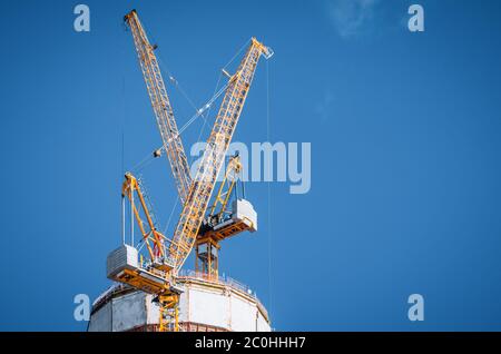 Two yellow cranes on top of a skyscraper under construction on a blue clear sky Stock Photo