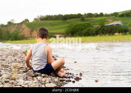 a village boy on the river Bank collects stones. Stock Photo