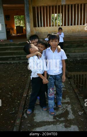 Vietnamese little boy pupils wear uniform: white t shirt, blue trousers standing with fun together on flooded school yard front of poor building Stock Photo