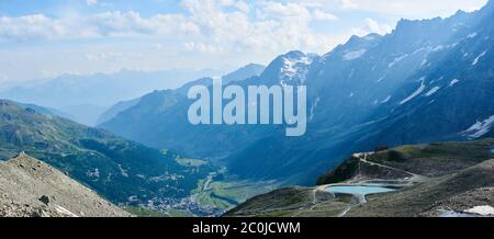 Magnificent panoramic view of hillside valley in Matterhorn or Monte Cervino mountains. Fantastic scenery of mountainous region with rocky crests, peaks, grassy hills and buildings under cloudy sky. Stock Photo