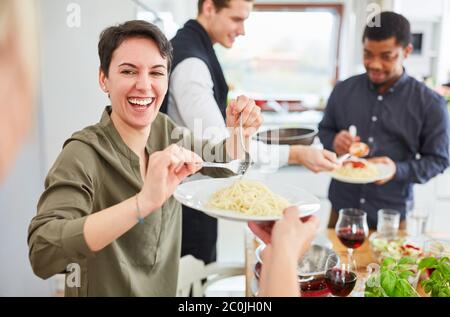 Young laughing woman serves pasta with tomato sauce in shared apartment for lunch Stock Photo