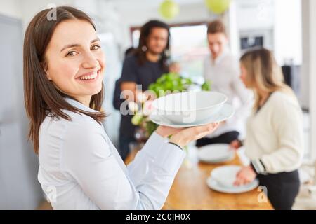 Young woman helps group at table setting by carrying dishes Stock Photo