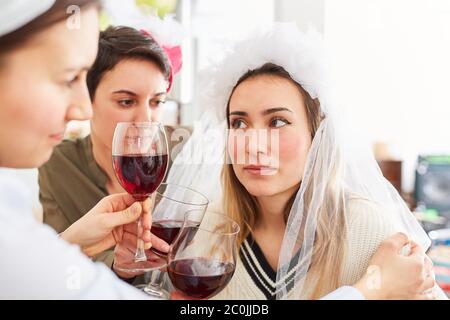 Friends consoling sad bride after a disappointed wedding with a glass of red wine Stock Photo