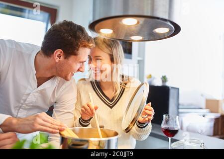 Happy couple together in kitchen while cooking spaghetti pasta on stove Stock Photo