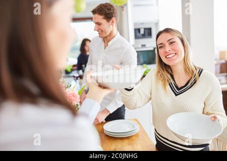 Friends with dishes together set the table for eating together in shared kitchen Stock Photo