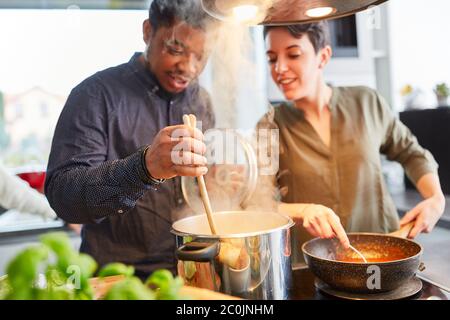 Friends cooking pasta with sauce together in shared kitchen for shared dining Stock Photo