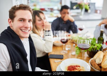 Happy friends eating pasta together at table while having meal together in kitchen Stock Photo