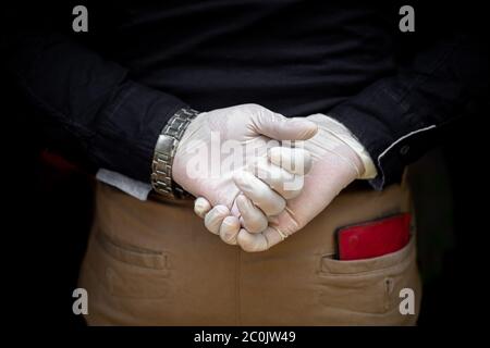 A man stands behind back with surgical gloves on both hands to protect against the coronavirus. Coronavirus disease safety purpose. Stock Photo