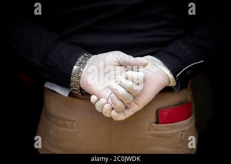 A man stands behind back with surgical gloves on both hands to protect against the coronavirus. Coronavirus disease safety purpose. Stock Photo