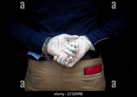 A man stands behind back with surgical gloves on both hands to protect against the coronavirus. Coronavirus disease safety purpose. Stock Photo