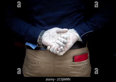 A man stands behind back with surgical gloves on both hands to protect against the coronavirus. Coronavirus disease safety purpose. Stock Photo