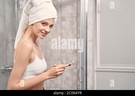 Smiling lovely lady with a cellphone standing in the bathroom Stock Photo