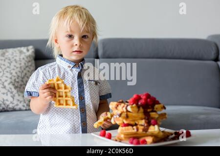 Sweet toddler birthday boy, eating belgian waffle with raspberries and chocolate at home Stock Photo