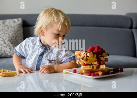Sweet toddler birthday boy, eating belgian waffle with raspberries and chocolate at home Stock Photo