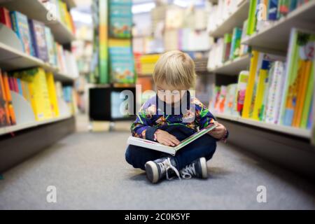 Adorable little boy, sitting in a book store and read book Stock Photo