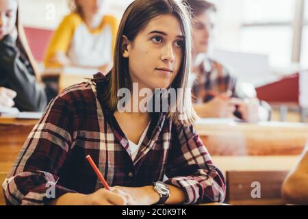 Beautiful teenage girl during a lecture in classroom. Female student paying attention in class and making notes. Stock Photo