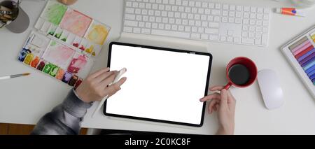 Overhead shot of female artist working with mock-up tablet, painting tools and drinking coffee on office desk Stock Photo