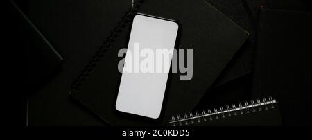 Top view of blank screen smartphone above black notebook on dark modern worktable Stock Photo