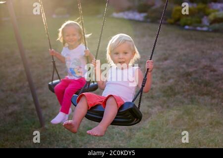 Sweet toddler children, swinging on swings on sunset in garden Stock Photo