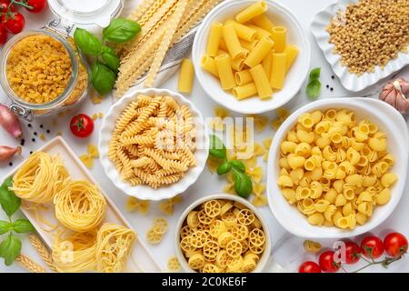 Variety of types and shapes of dry pasta - fusilli, penne, fettuccine nests, mafaldine, shells, bowtie and wheels - in white bowls with traditional It Stock Photo