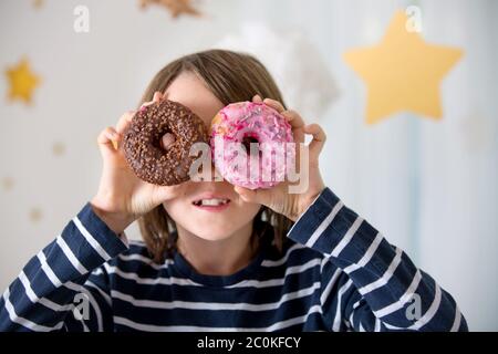 Cute sweet blonde child, playing and eating donuts at home Stock Photo