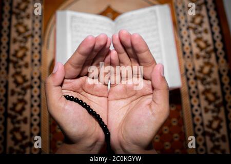 Young Muslim woman praying with Tasbeeh. The Holy Quran is the background, Indoors. Focus on hands. Stock Photo