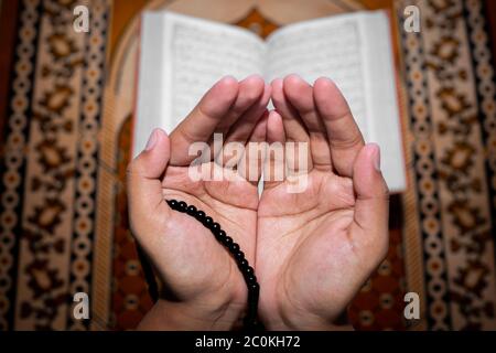 Young Muslim woman praying with Tasbeeh. The Holy Quran is the background, Indoors. Focus on hands. Stock Photo