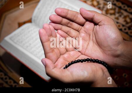 Young Muslim woman praying with Tasbeeh. The Holy Quran is the background, Indoors. Focus on hands. Stock Photo