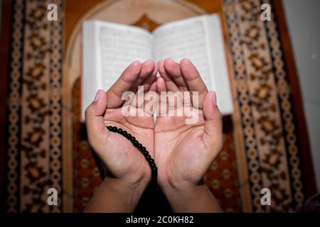 Young Muslim woman praying with Tasbeeh. The Holy Quran is the background, Indoors. Focus on hands. Stock Photo