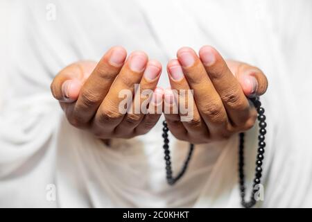 Muslim women raise their hands to pray with a Tasbeeh on white background, indoors. Focus on hands. Stock Photo