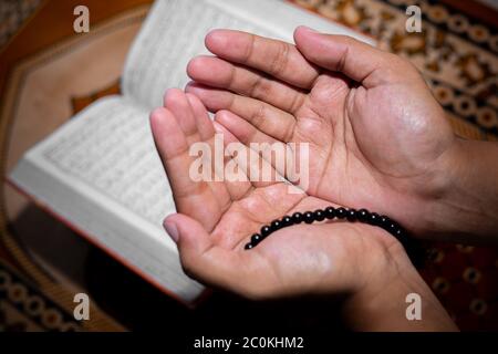 Young Muslim woman praying with Tasbeeh. The Holy Quran is the background, Indoors. Focus on hands. Stock Photo