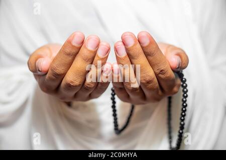 Muslim women raise their hands to pray with a Tasbeeh on white background, indoors. Focus on hands. Stock Photo