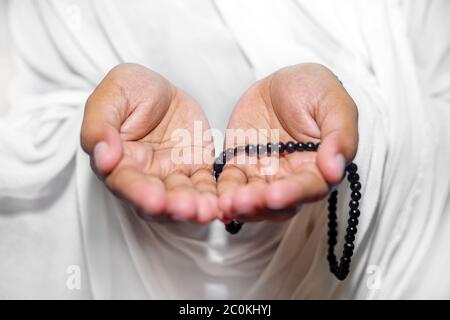 Muslim women raise their hands to pray with a Tasbeeh on white background, indoors. Focus on hands. Stock Photo