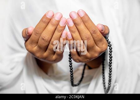 Muslim women raise their hands to pray with a Tasbeeh on white background, indoors. Focus on hands. Stock Photo