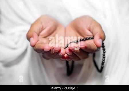 Muslim women raise their hands to pray with a Tasbeeh on white background, indoors. Focus on hands. Stock Photo