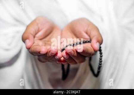 Muslim women raise their hands to pray with a Tasbeeh on white background, indoors. Focus on hands. Stock Photo