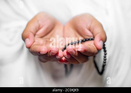 Muslim women raise their hands to pray with a Tasbeeh on white background, indoors. Focus on hands. Stock Photo