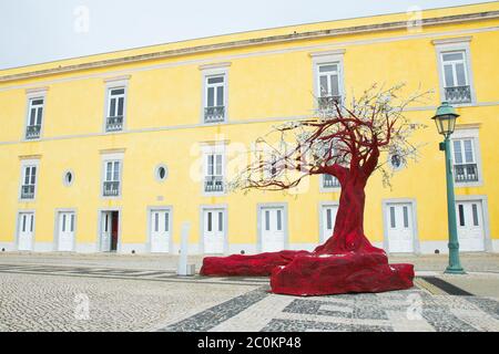 Red tree, Cascais, Portugal. Beautiful piece of art. Yellow building in the background, the Pousada historic Pestana Cidadela luxury hotel & art Stock Photo