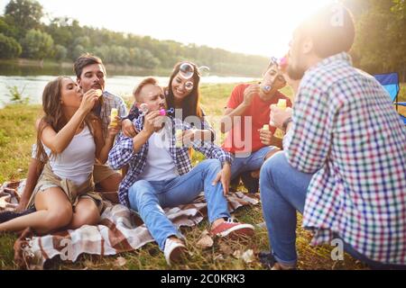 Young people make soap bubbles while sitting on the grass on in nature. Stock Photo