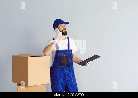 Positive courier with carton boxes talking on smartphone, getting new delivery order against grey background. Mockup for design Stock Photo