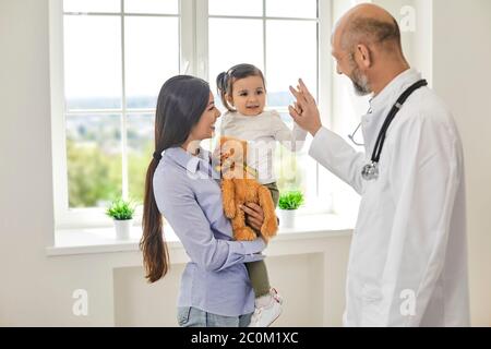Family doctor.Senior doctor giving high five to girl at medical office. Little patient with her mommy on visit to pediatrician Stock Photo