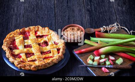 Homemade Strawberry Rhubarb Pie on a dark wooden kitchen table with ingredients, landscape view, free space Stock Photo