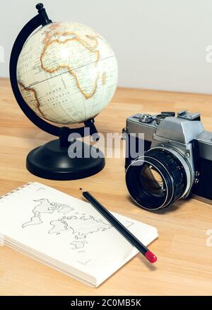 Camera, world globe and notebook with world map on a wooden desk. Travel concept image: planning a journey.