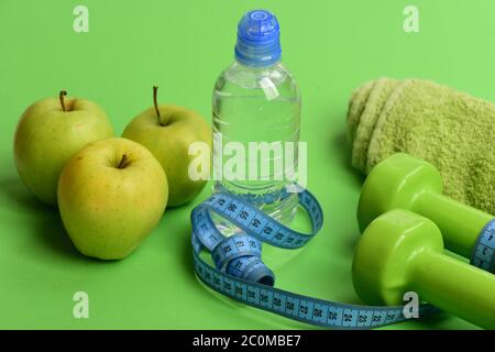 Barbells near juicy green apples. Healthy lifestyle equipment, close up. Diet and sport regime concept. Dumbbells in bright green color, water bottle, measure tape, towel and fruit on green background Stock Photo